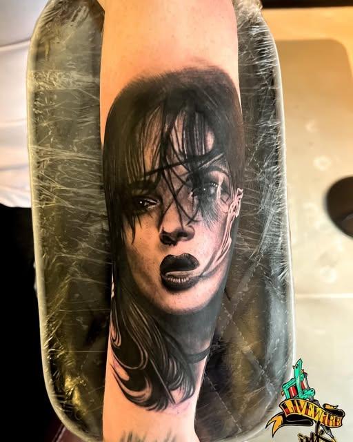 Freshly healed black and grey portrait tattoo of a woman with dark lips and scratched linework, wrapped on a forearm