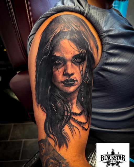Black and grey realism portrait tattoo of a woman on an upper arm, by Blackstar Tattoo Studio Belfast